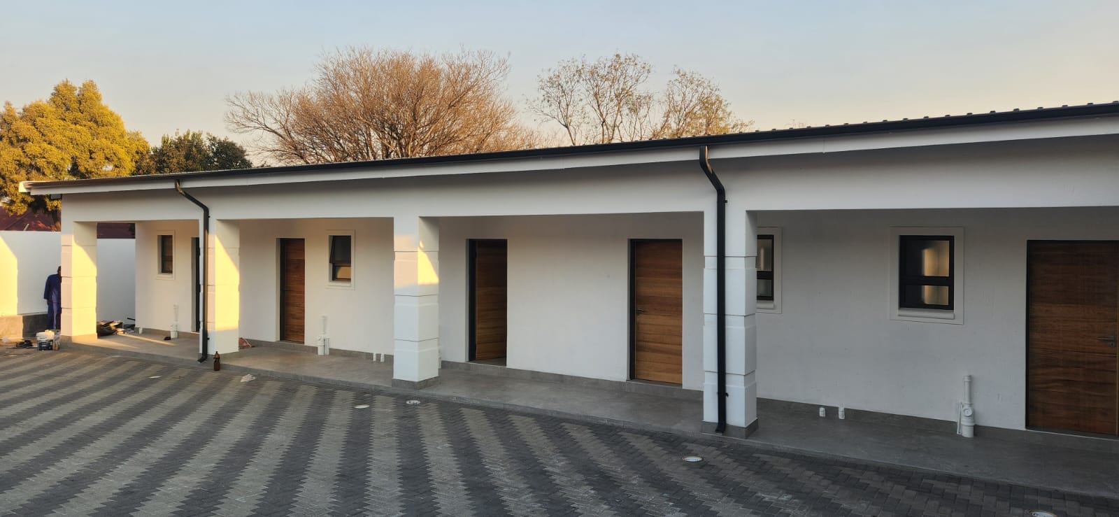 Black gutter line and downpipes along a row of townhouse units at golden hour